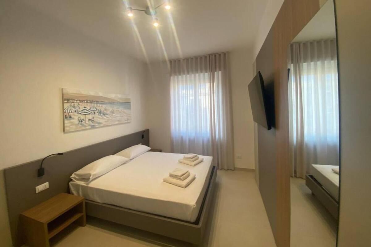 A modern hotel room with a bed, bedside table, artwork, curtains, and a TV.