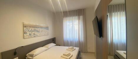 A modern hotel room with a bed, bedside table, artwork, curtains, and a TV.