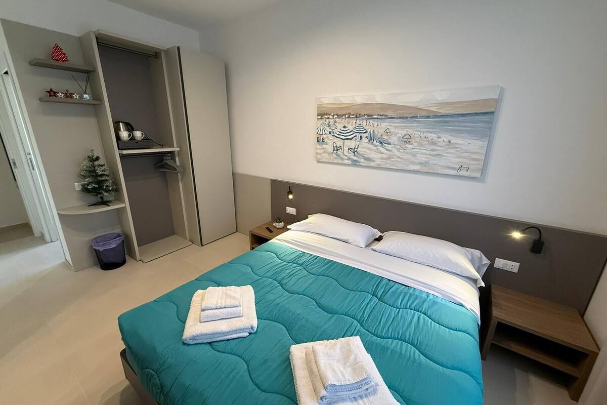 A bedroom with a bed, a nightstand, a wall-mounted lamp, a painting, and a wardrobe.