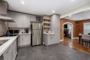 A modern kitchen with grey cabinets, stainless steel appliances, and a dining area with a wooden floor. - 2BR Home Near MD Anderson & TMC | Sleeps 6 | Hot Tub | Free Parking (Houston)