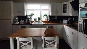 A compact kitchen with white cabinets, a wooden countertop, and a dining area with two white chairs. - Cosy Home With Organic Garden (Athenry)