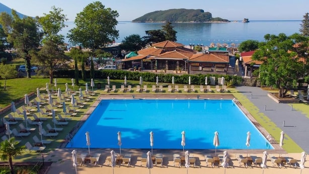 A resort with a large swimming pool, sun loungers, and a view of the sea and a mountain. - Hotel Aleksandar (Budva)