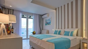 A modern hotel room with a large bed, a desk with a lamp, and a view of the outdoors through a sliding door. - Hotel Aleksandar (Budva)