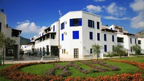 A white building with blue accents, a well-maintained garden with colorful flowers, and a clear blue sky. - Hotel Aleksandar (Budva)