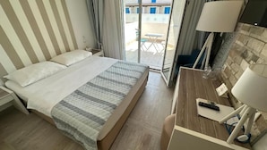 A hotel room with a bed, a desk with a lamp, and a view of the outside balcony. - Hotel Aleksandar (Budva)
