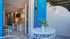 A cozy outdoor seating area with a white metal table and chairs, a blue shutter door, and a stone wall backdrop. - Hotel Aleksandar (Budva)