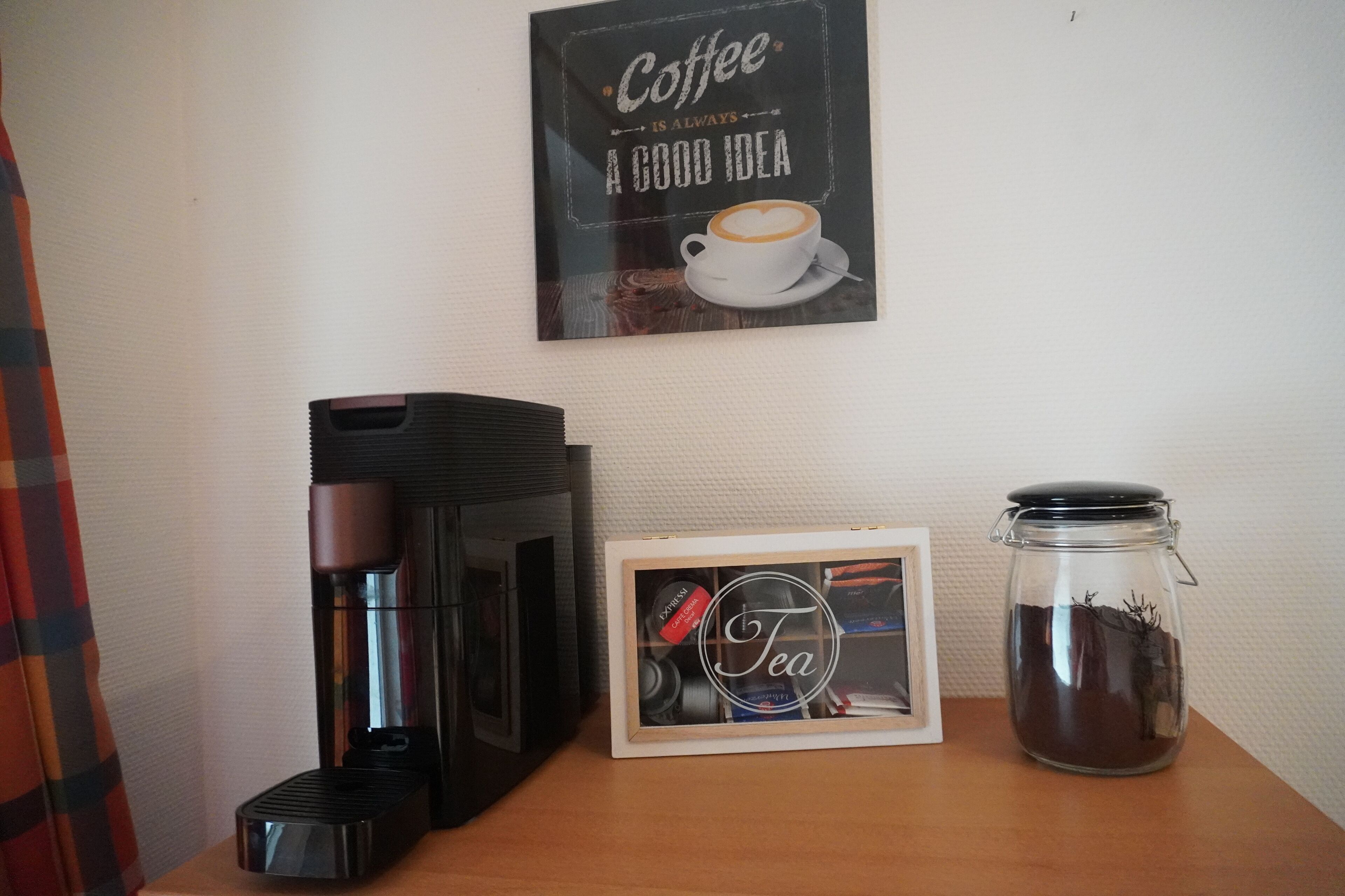 En kaffebryggare, en teburk i en ram och en glasburk med te på ett träbord.