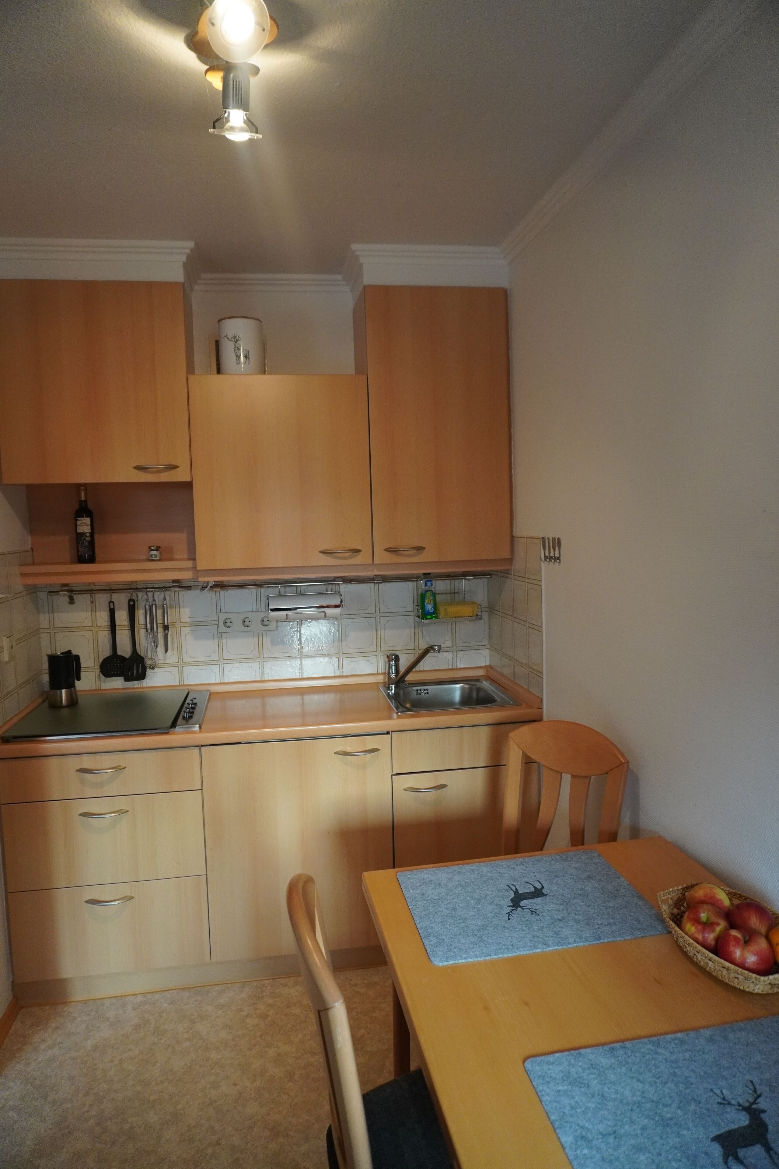 Een compacte keuken met houten kastjes, een gootsteen en een eethoek met een tafel en stoelen.