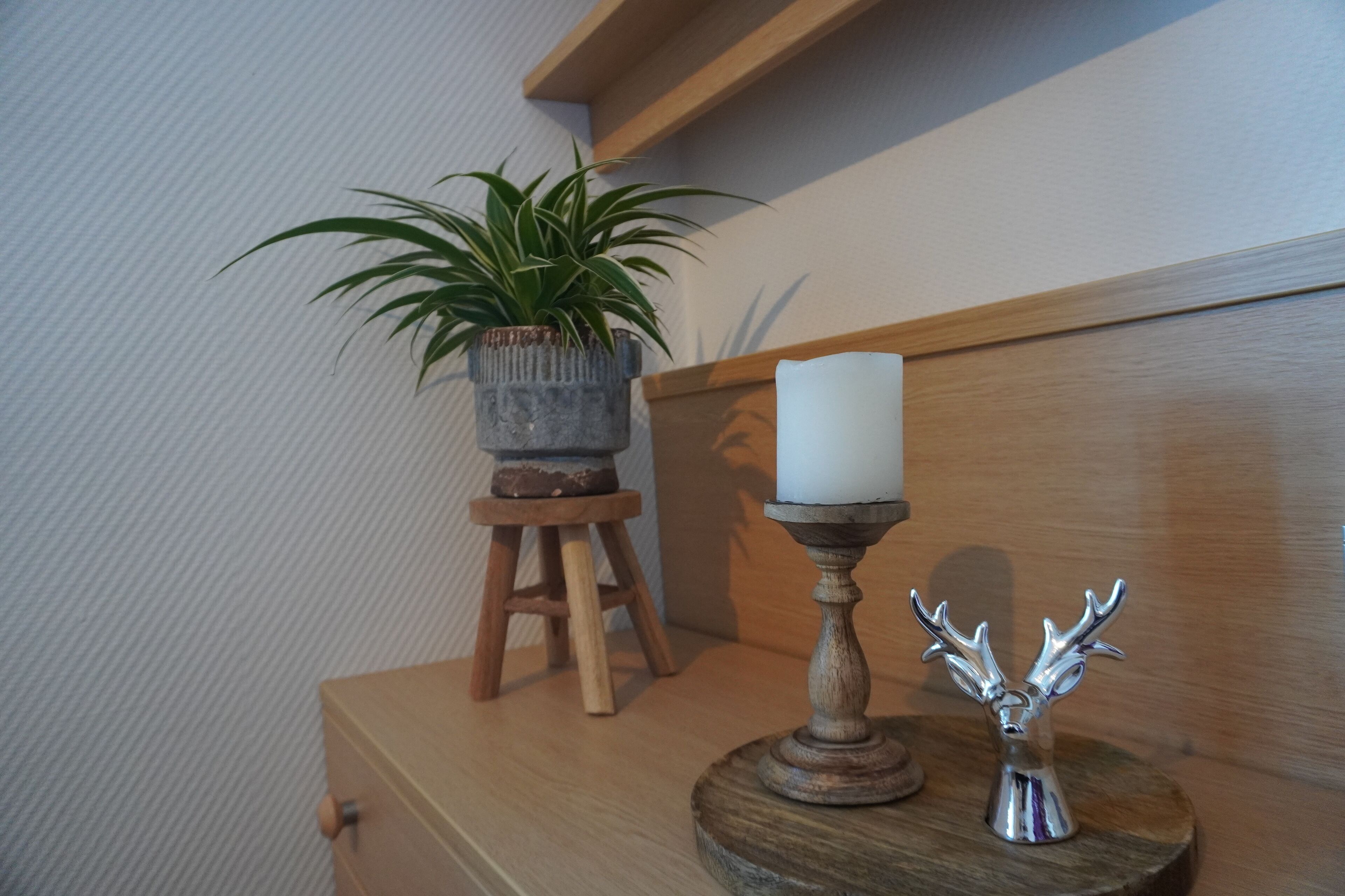 En byrå i trä med en krukväxt, ett ljus och en liten statyett av en hjort i silver.