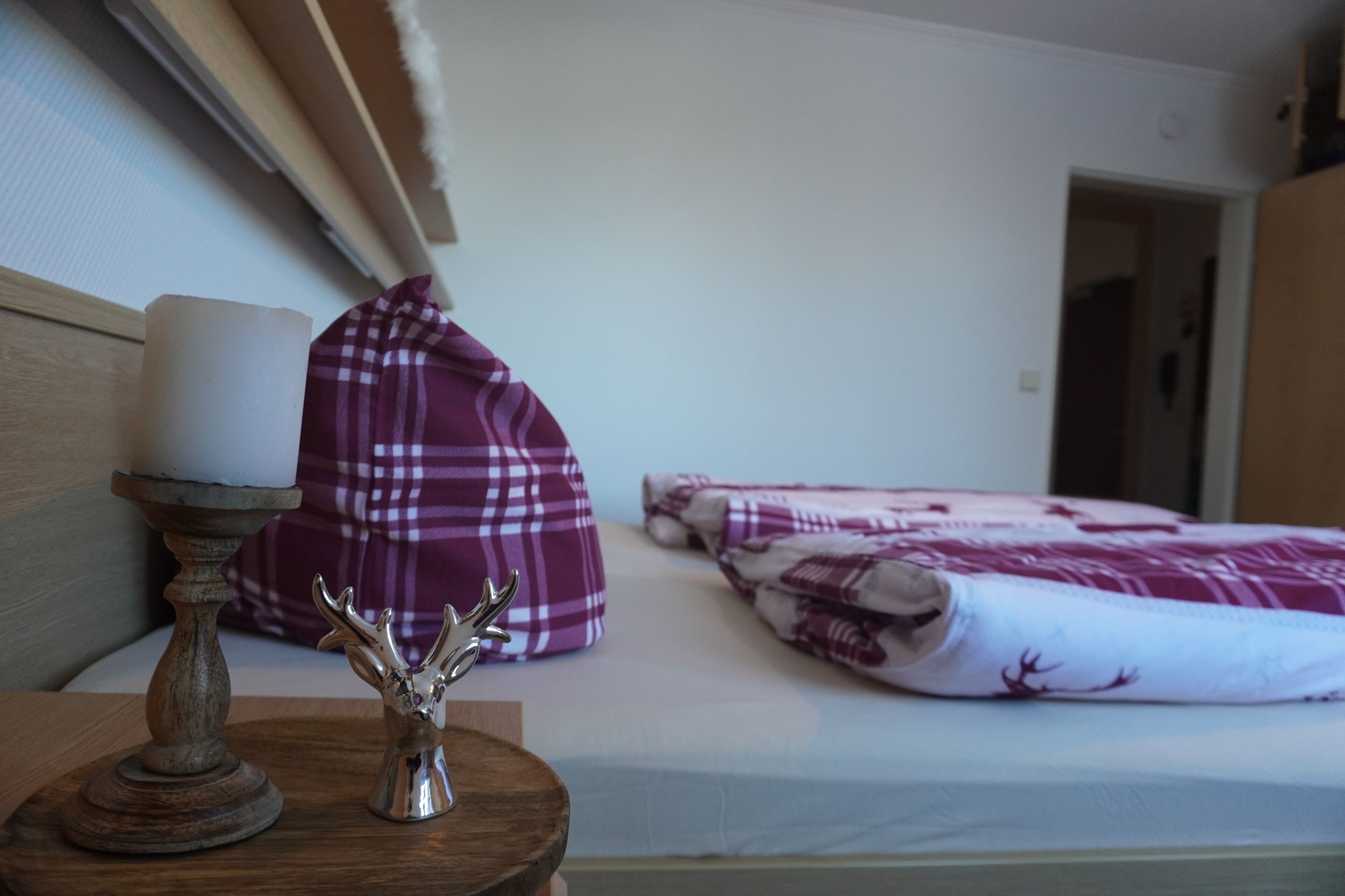 Un dormitori amb un llit, una taula de nit amb una espelma i un objecte decoratiu, i una manta de llanes morada.