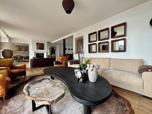 Een moderne woonkamer met een ronde salontafel, leren fauteuils, een beige bank en een bijzettafeltje van steen.