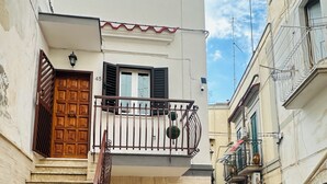 Un edificio a due piani con una porta in legno, un balcone con ringhiera in metallo e una pianta in vaso al piano terra.