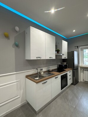 A modern kitchen with white cabinets, a wooden countertop, stainless steel appliances, and a blue accent wall. - The Arch House nr 45 (Triggiano)