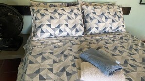 Una cama con ropa de cama estampada, un ventilador de pared y una decoración con girasol.