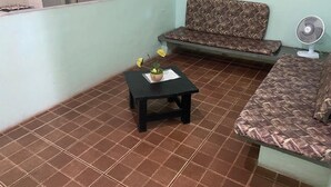 Un salón con un sofá estampado, una mesita negra con una planta y un ventilador.