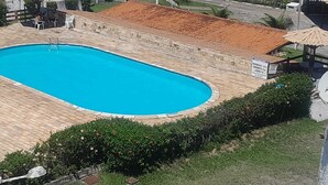 Una piscina con borde de baldosas, rodeada de follaje y un edificio con techo de tejas.