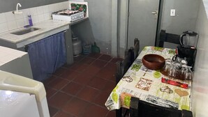 Cocina compacta con estufa a gas, lavamanos y mesa de comedor con mantel.