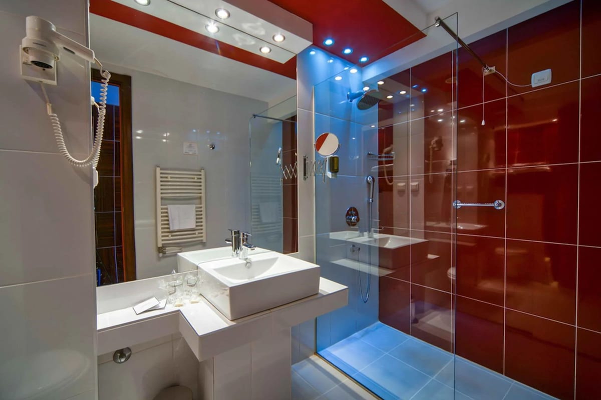 Un baño moderno con cabina de ducha de vidrio, un lavabo blanco y un secador de pelo montado en la pared.