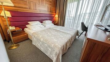 A hotel room with a wooden headboard, a large bed with white linens, a desk with a computer, and a chair.