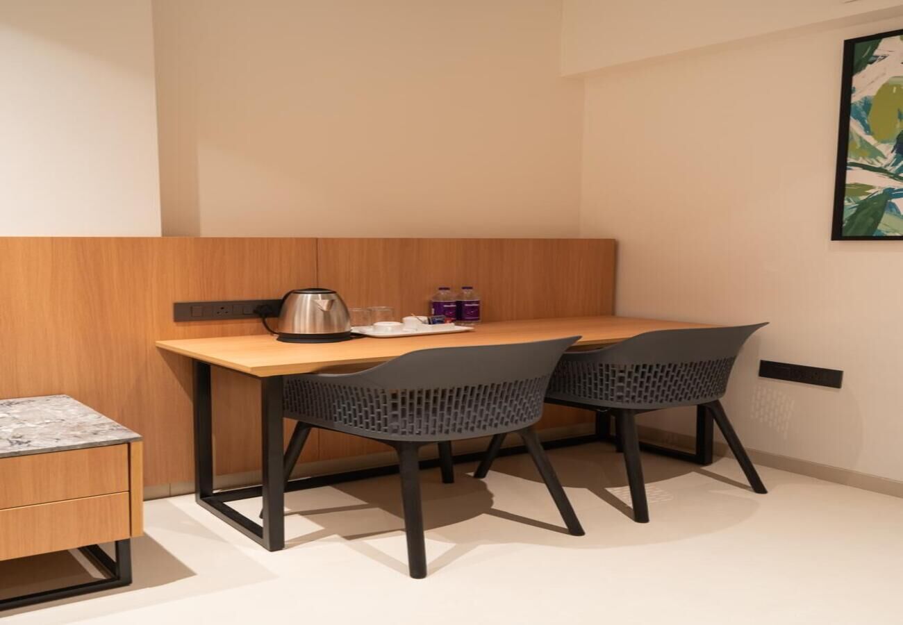 Une pièce de taille modeste, avec une table en bois et deux chaises, un petit meuble et une prise de courant fixée au mur.