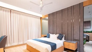 A modern bedroom with a large bed, a bedside table, a desk, and a chair. - Airotel (Pune)