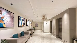 A modern hotel lobby with a marble floor, a sofa with teal cushions, and artwork on the walls. - Airotel (Pune)