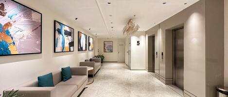 A modern hotel lobby with a marble floor, a sofa with teal cushions, and artwork on the walls.