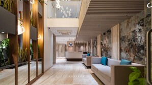 A modern hotel lobby with a reception desk, a seating area with sofas, and a decorative wall with plants. - Airotel (Pune)