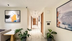 A modern hallway with a marble floor, potted plants, framed artwork, and a sofa. - Airotel (Pune)