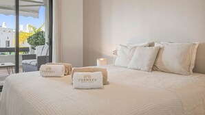 A hotel room with a large bed, two pillows, a bedside table with a lamp, and a view of the city through a large window. - Perla Del Sol Estepona (Estepona)
