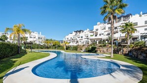 A swimming pool with a curved design, surrounded by well-maintained grass and palm trees. - Perla Del Sol Estepona (Estepona)