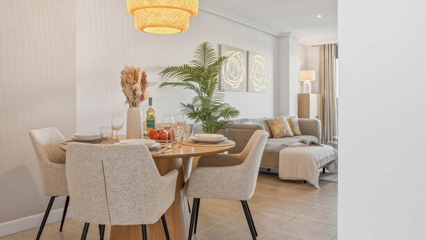 A dining area with a round table, four chairs, a hanging light fixture, and a potted plant. - Perla Del Sol Estepona (Estepona)