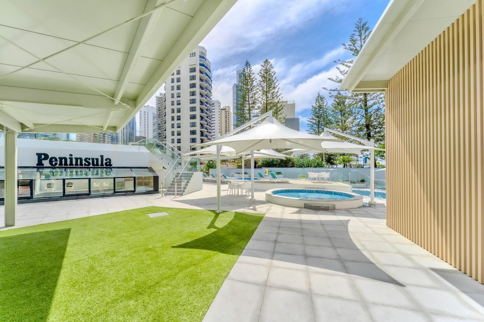 Uma área moderna de piscina ao ar livre com um espaço de estar coberto, uma piscina pequena e um edifício com a inscrição "Peninsula" ao fundo.