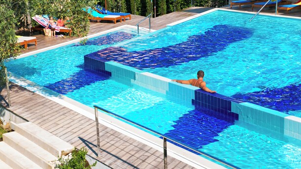 En swimmingpool med kakelbeklädda trappsteg som leder ner i vattnet, omgiven av solstolar och ett trädäck.