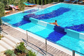 A swimming pool with tiled steps leading into it, surrounded by lounge chairs and a wooden deck. - Hotel Castellastva (Petrovac)