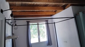 Een kamer met een houten plafond, een raam met gordijnen en een metalen bed.
