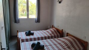 Een kamer met twee eenpersoonsbedden, een raam met gordijnen, een wandlamp en een deur.