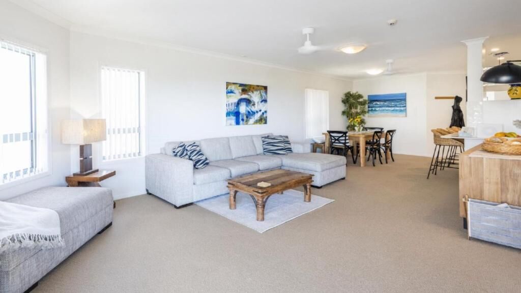 A spacious living area with a grey sofa, wooden coffee table, and a dining table with chairs.