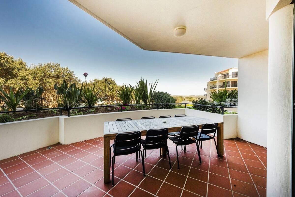 Una terraza con mesa y sillas, rodeada de un suelo de baldosas y una barandilla.