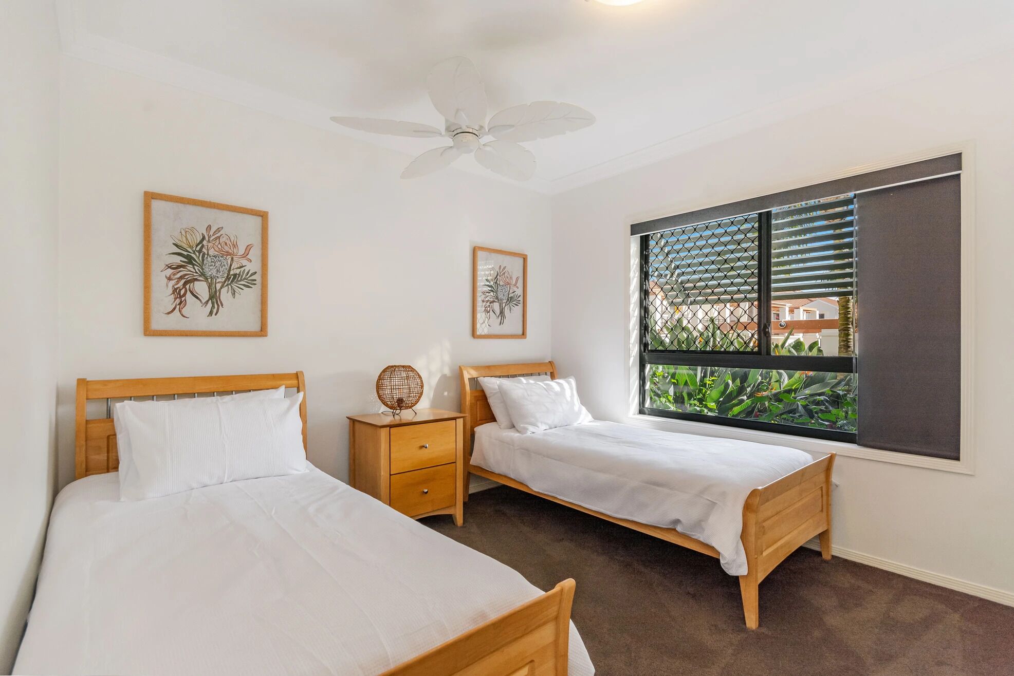A bedroom with two single beds, a ceiling fan, and a window with a view of greenery.