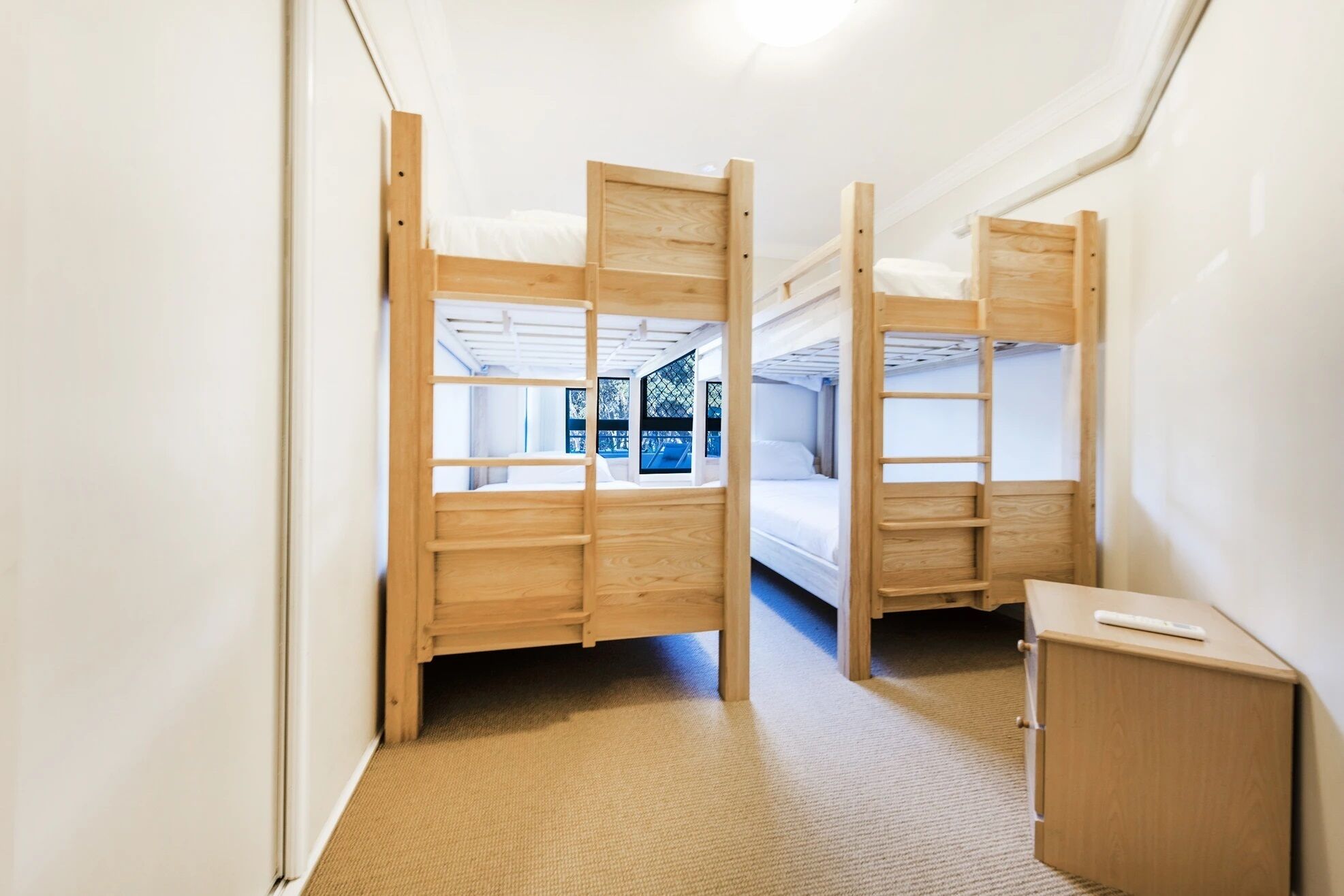 Une petite pièce comprenant deux lits superposés, une petite armoire en bois et une fenêtre donnant sur un bâtiment extérieur.