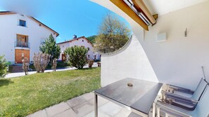 Une terrasse avec une table et des chaises, un mur blanc et une vue sur un immeuble doté d’un balcon.