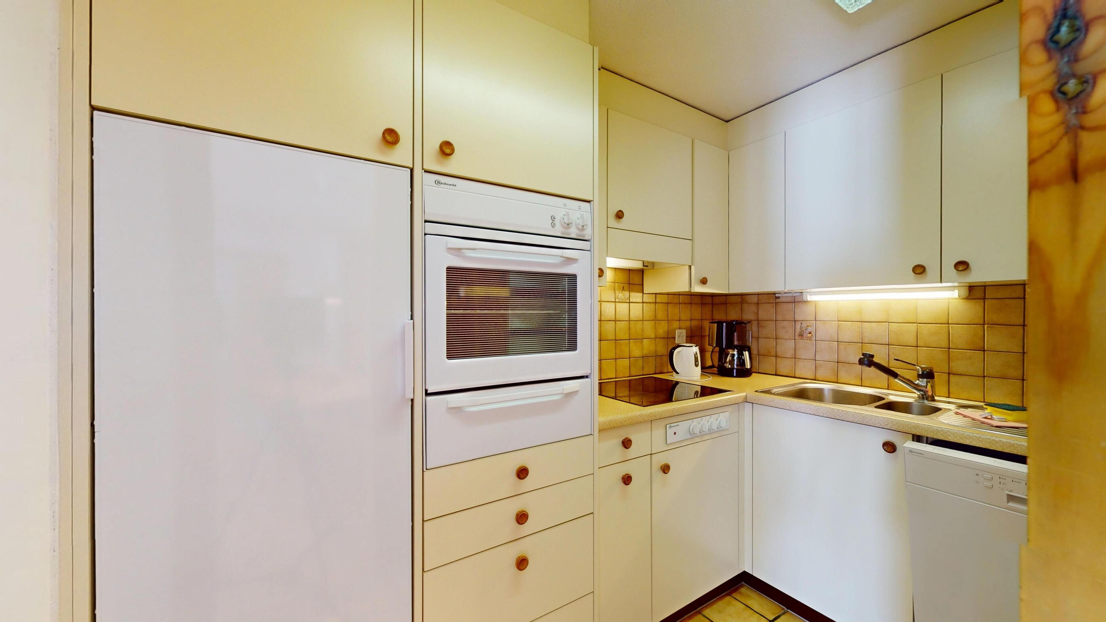 A compact kitchen with white appliances, a tiled backsplash, and a sink.