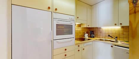A compact kitchen with white appliances, a tiled backsplash, and a sink.