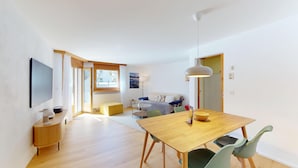 Un apartamento moderno con una mesa de comedor de madera, un sofá y un televisor montado en la pared.