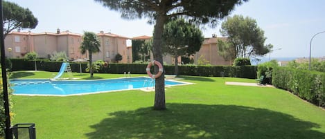 A swimming pool with a slide, surrounded by well-maintained grass and a tree.