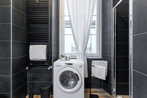A compact bathroom with a washing machine, a towel rack, a trash bin, and a window with curtains. - Residence in Como with 1 bedrooms sleeps 4 (Como)