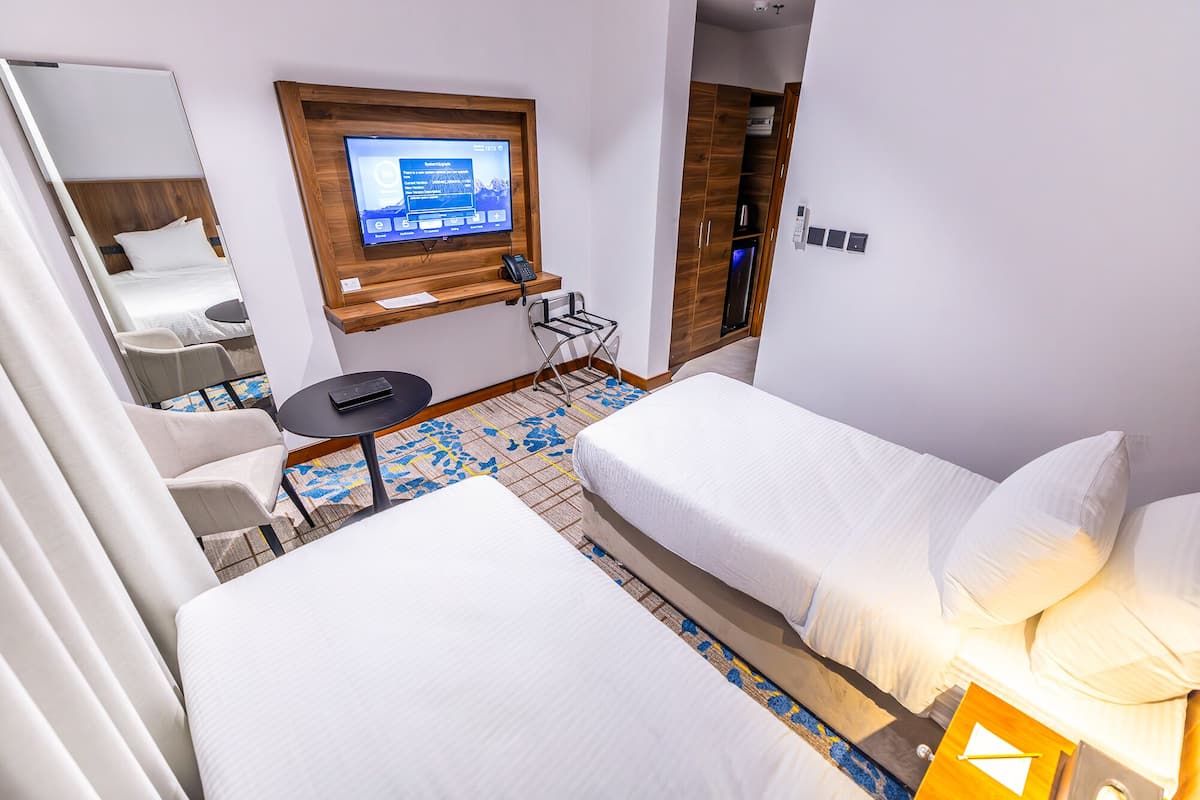 A hotel room with two beds, a desk with a computer, a TV mounted on the wall, and a wardrobe.