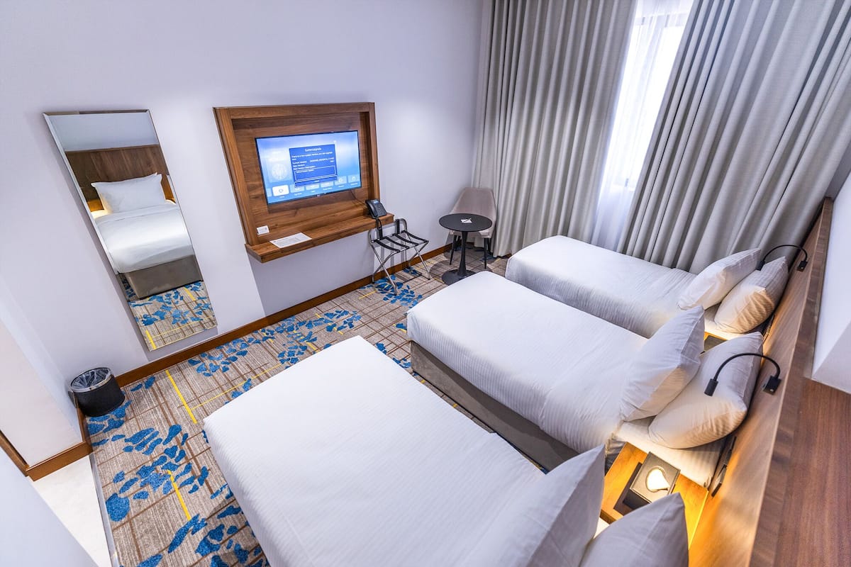 A hotel room with two beds, a desk with a computer, a chair, a small table, and a mirror.
