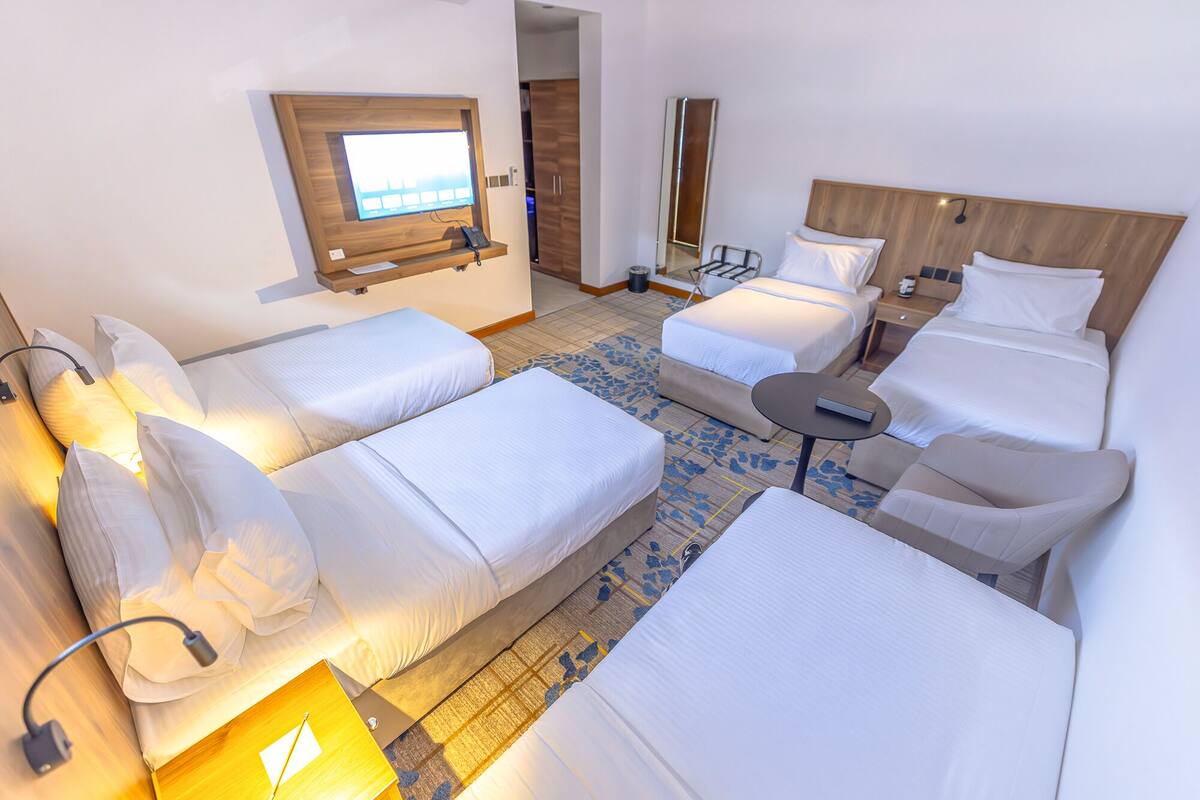 A hotel room with two single beds, a double bed, a small table, and a TV mounted on the wall.